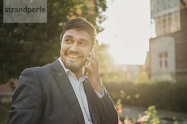 Lächelnder Geschäftsmann  der im Park mit dem Smartphone spricht