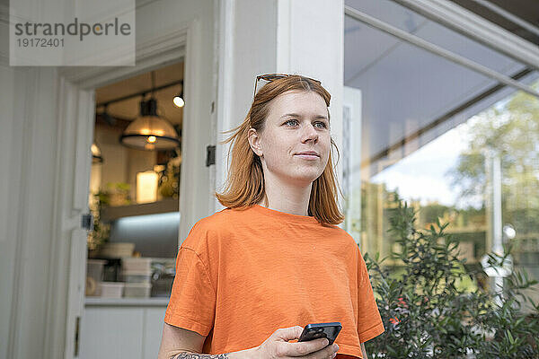 Nachdenkliche Frau mit Mobiltelefon im Straßencafé