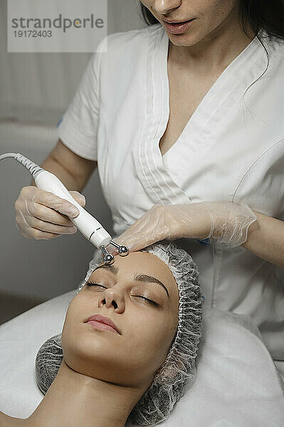 Junger Dermatologe massiert mit Geräten die Stirn einer Frau