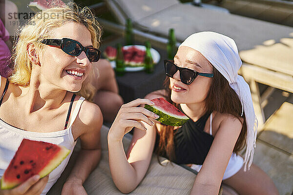 Fröhliche Freunde halten Wassermelone in der Hand und entspannen sich an einem sonnigen Tag gemeinsam