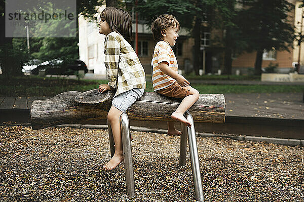 Playful boys sitting on outdoor play equipment in park