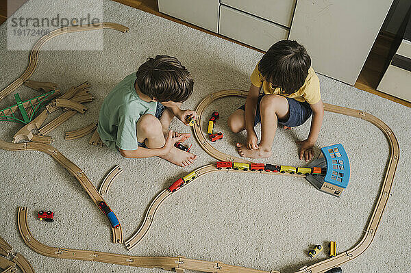 Jungen spielen zu Hause mit einer Spielzeugeisenbahn auf dem Teppich