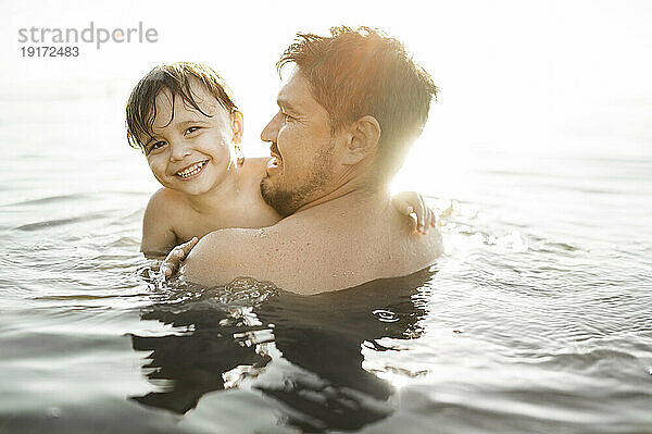 Glücklicher Vater mit Sohn  der an einem sonnigen Tag im Wasser schwimmt