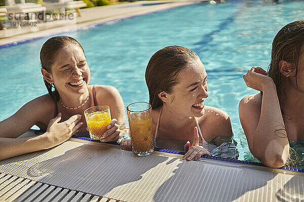Fröhliche Freunde mit Gläsern Saft feiern an einem sonnigen Tag im Schwimmbad