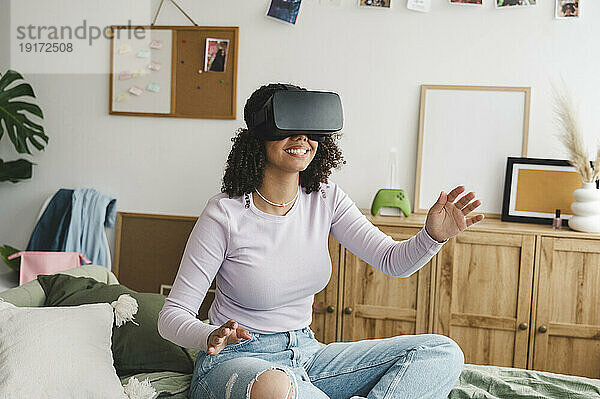 Fröhliches Mädchen mit Virtual-Reality-Simulatoren gestikuliert zu Hause im Bett