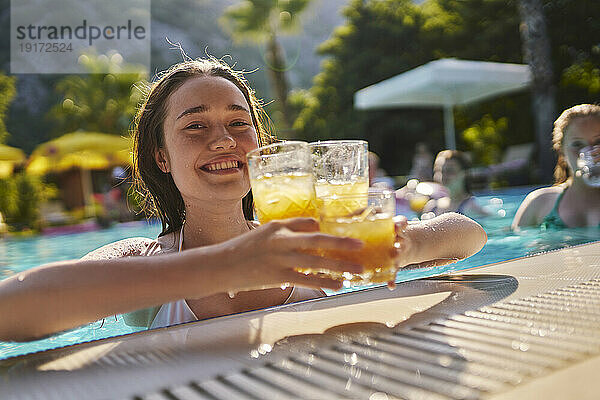Glückliche Frau hält an einem sonnigen Tag Gläser Orangensaft im Pool