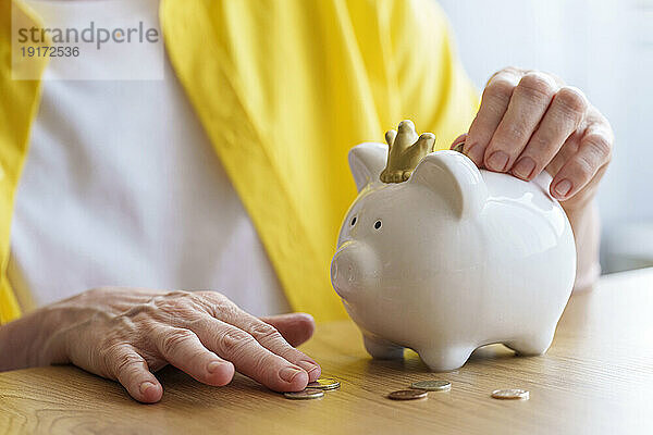 Hände einer älteren Frau  die Geld im Sparschwein spart