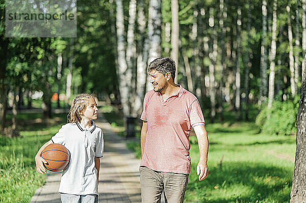 Junge mit Basketball spricht mit Vater und geht im Park spazieren