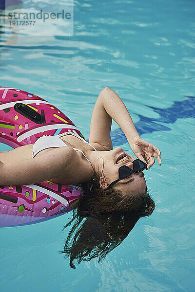 Teenager-Mädchen mit Sonnenbrille liegt auf Schwimmschlauch im Pool