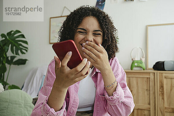Cheerful girl using smart phone at home