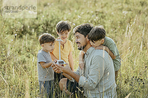 Lächelnder Vater zeigt Kindern auf dem Feld das Modell einer Windkraftanlage