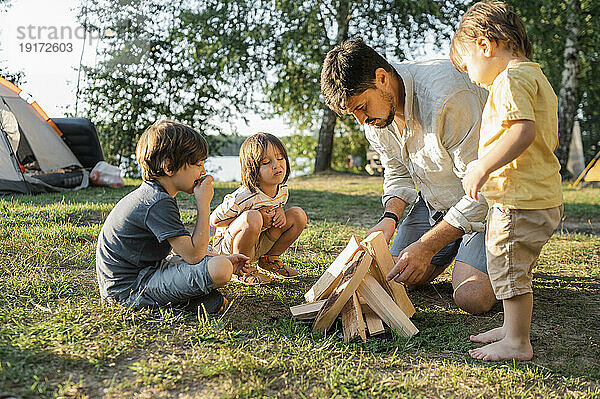 Vater und Kinder bereiten sich an einem sonnigen Tag mit Holz auf das Lagerfeuer vor