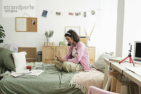 Smiling teenage girl using mobile phone on bed at home