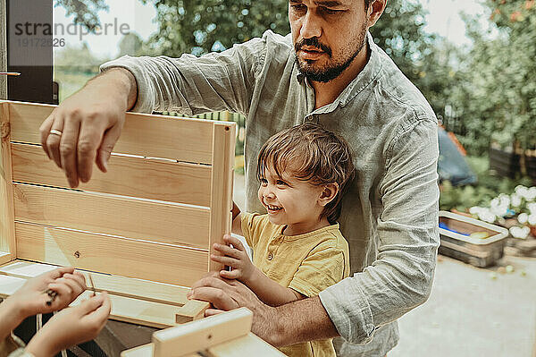 Vater hilft glücklichen Söhnen bei der Herstellung einer Holzkiste im Hinterhof