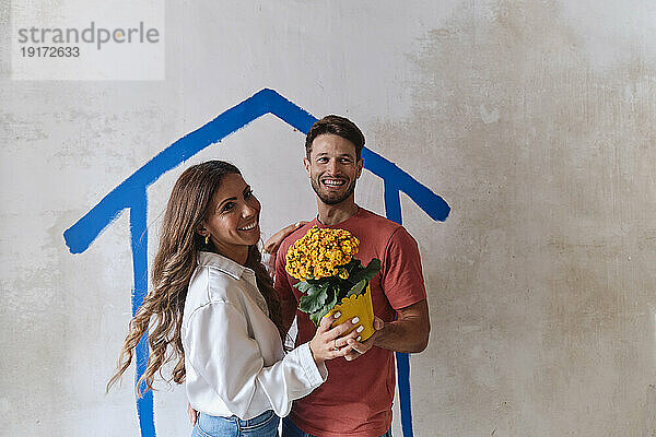 Fröhliches Paar hält Blumenstrauß vor der Wand vor Ort
