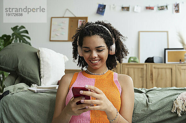 Fröhliches Teenager-Mädchen benutzt Mobiltelefon im Schlafzimmer