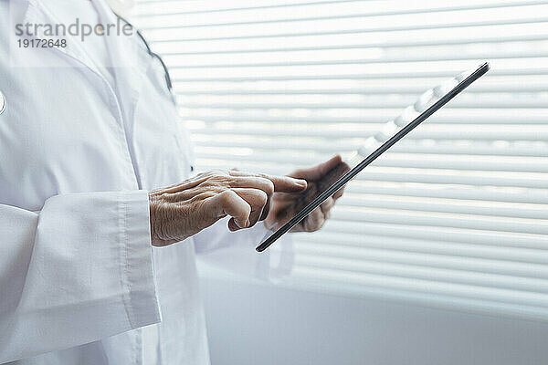 Hände eines leitenden Arztes  der einen Tablet-PC am Fenster verwendet