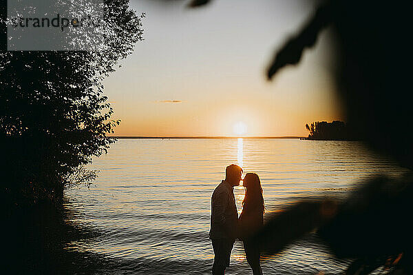 Mann umarmt Frau vor dem Meer bei Sonnenuntergang
