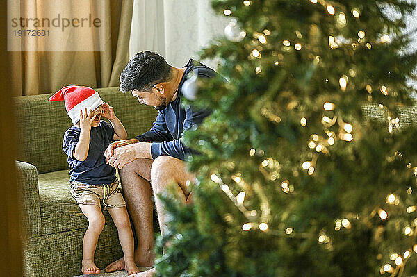 Vater und Sohn amüsieren sich auf dem Sofa neben dem Weihnachtsbaum