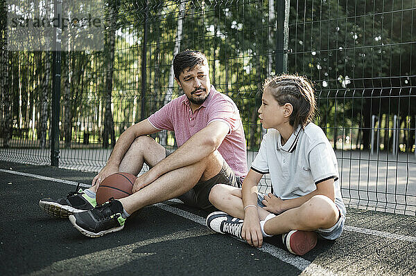 Father and son talking in basketball court