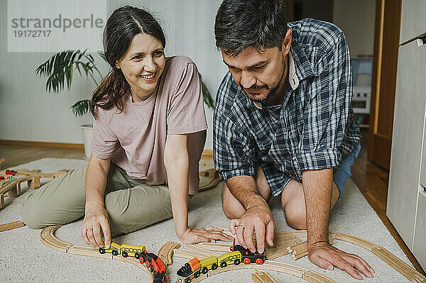 Happy man and woman playing with toy train on carpet at home