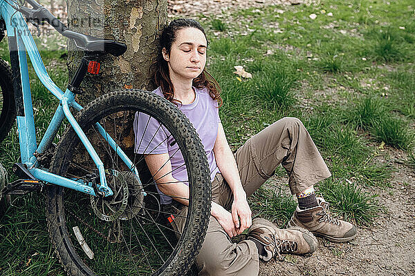 Junge Frau macht Pause neben Fahrrad unter Baum im Wald