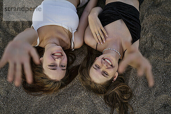 Happy young women lying on sand with hands raised