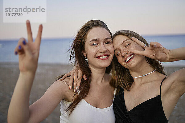 Fröhliche junge Freunde gestikulieren am Strand mit einem Friedenszeichen