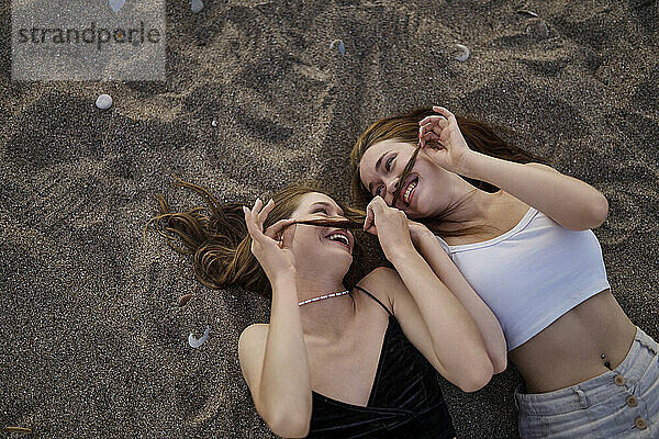 Glückliche Frauen machen Schnurrbart mit Haaren und liegen auf Sand