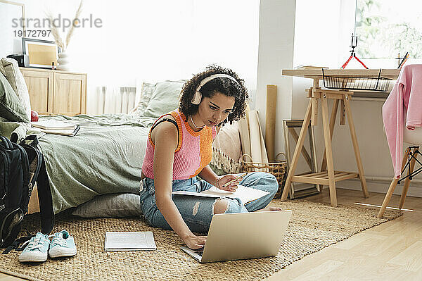 Lockenhaariges Teenager-Mädchen benutzt Laptop und macht zu Hause Hausaufgaben
