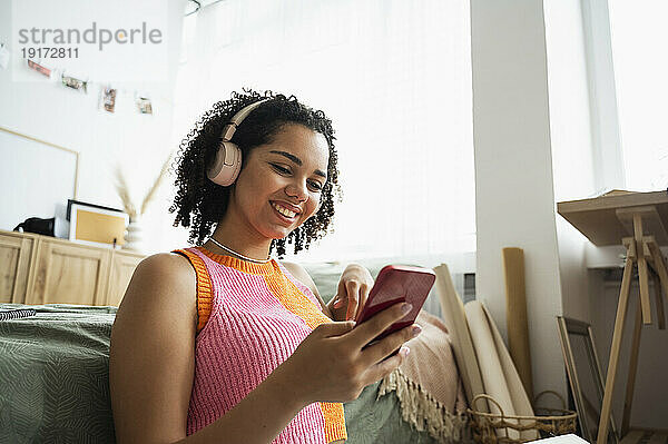 Lächelndes Teenager-Mädchen benutzt Mobiltelefon im Schlafzimmer zu Hause