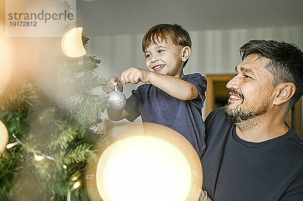 Lächelnder Vater und Sohn schmücken zu Hause den Weihnachtsbaum