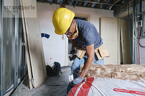 Reifer Bauarbeiter mit Schutzhelm arbeitet vor Ort mit Isolierung
