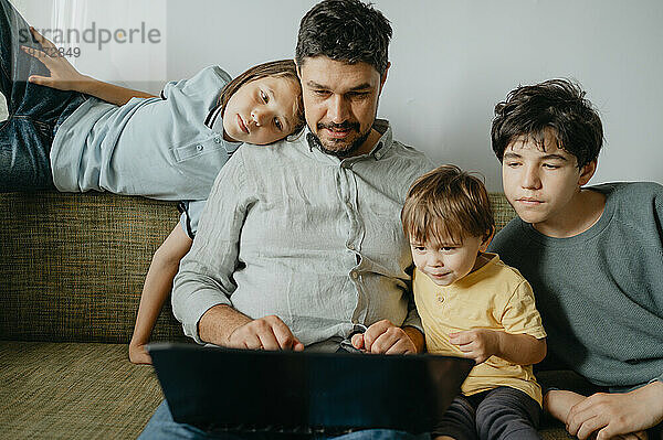 Kinder mit Vater  der zu Hause Laptop benutzt