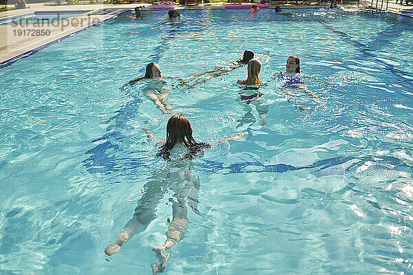 Freunde schwimmen an einem sonnigen Urlaubstag gemeinsam im Pool