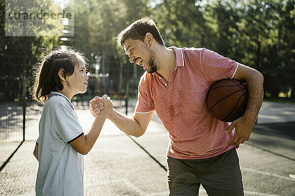 Glücklicher Vater mit Basketball  der die Hand seines Sohnes vor Gericht hält