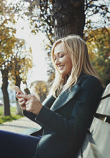 Lächelnde Frau mit Smartphone auf Bank sitzend