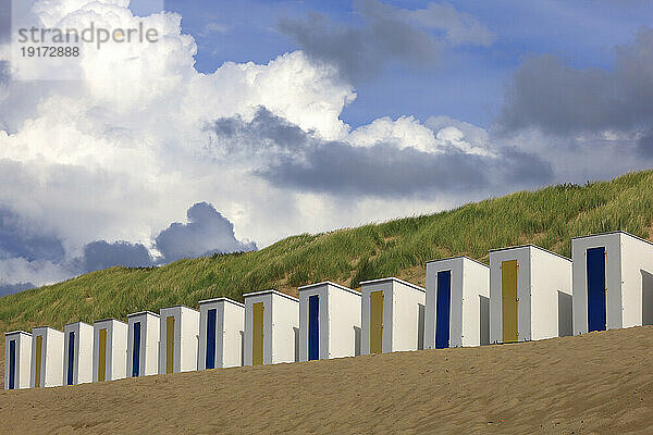 Reihe von Strandhütten mit grasbewachsener Düne im Hintergrund