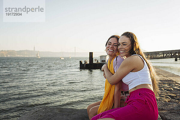 Glückliche Frau umarmt Freundin  die auf der Promenade sitzt