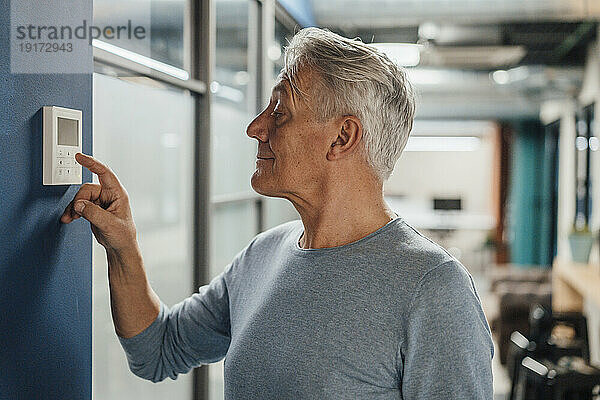 Lächelnder älterer Geschäftsmann nutzt digitalen Thermostat am Arbeitsplatz
