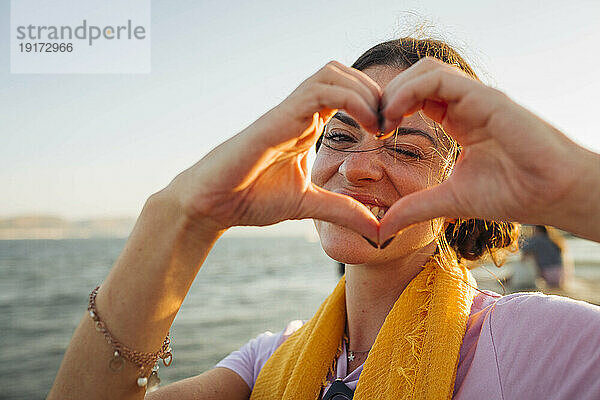 Smiling woman gesturing heart shape at the waterfront