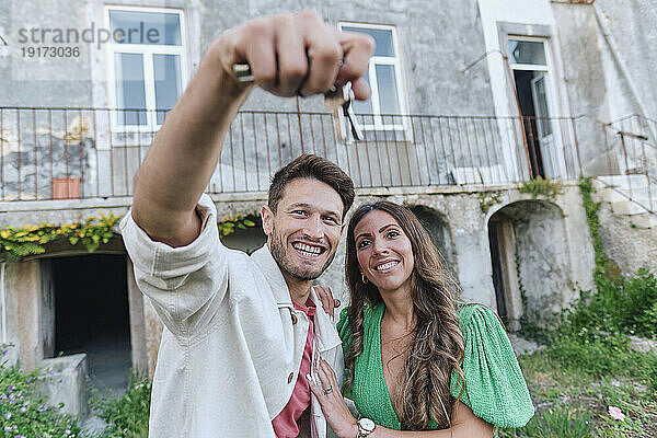 Glückliches Paar mit Schlüsseln  das zusammen vor dem Haus steht