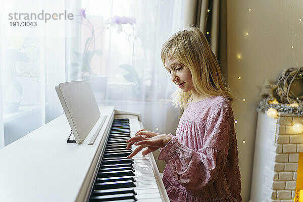 Blondes Mädchen spielt an Weihnachten zu Hause Klavier