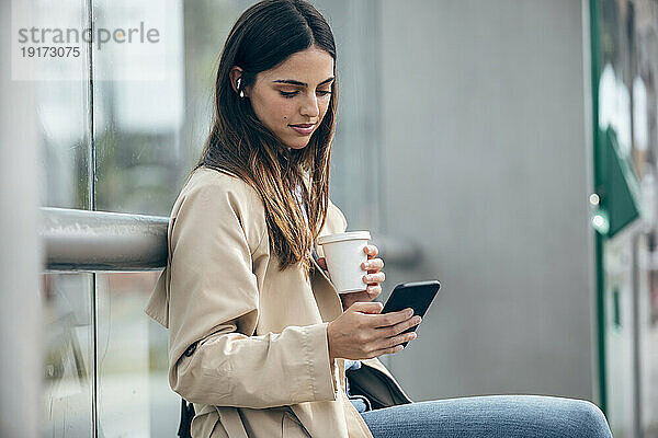 Junge Frau mit Kaffeetasse und Smartphone