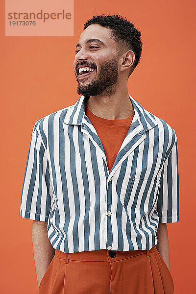 Smiling man wearing striped shirt standing against orange background
