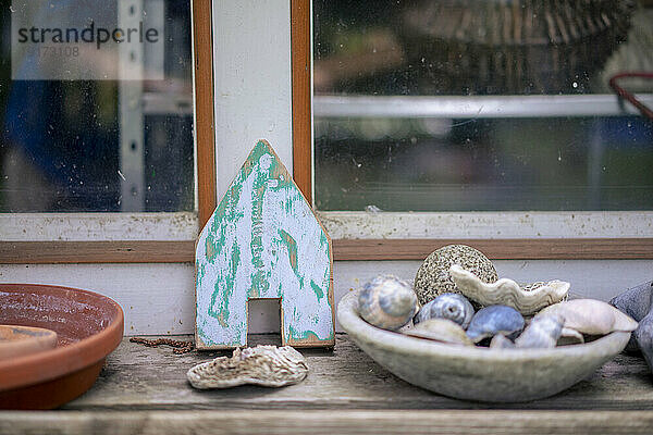 Various sea shells in bowl with model house on table near window