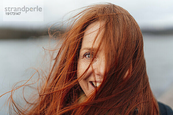 Lächelnde rothaarige Frau mit wehenden Haaren im Gesicht