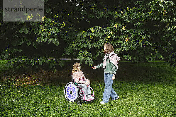 Tochter sitzt im Rollstuhl neben Mutter im Park
