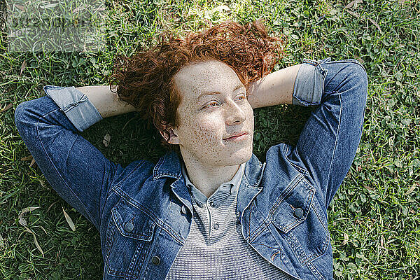 Nachdenklicher junger Mann mit den Händen hinter dem Kopf entspannt sich im Gras