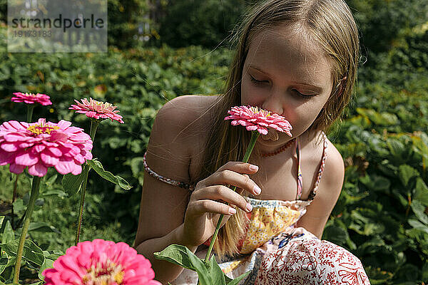 Blondes Mädchen riecht rosa Blume im Garten